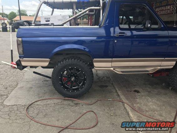 Side view of a blue 1996 Ford Bronco with aftermarket wheels and tires, and a roll cage