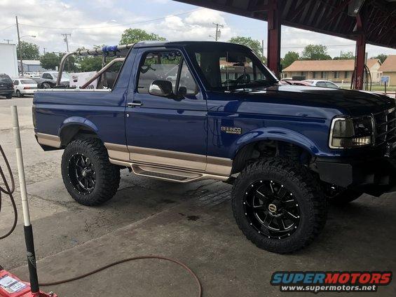 Blue 1996 Ford Bronco with tan trim and aftermarket black wheels parked under a covered area