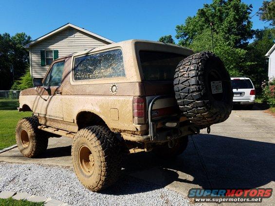 Rear view of a mud-covered 1988 Ford Bronco with a spare tire on the back. License plate visible