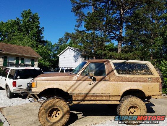 Mud-covered 1988 Ford Bronco parked next to a white SUV