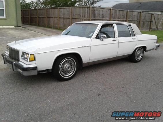 white sedan parked on asphalt, wooden fence behind it