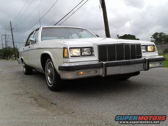 White sedan front view, wire wheels, chrome bumper, vertical grille, cloudy sky