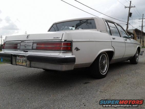 rear view of a white 1980s sedan with wire wheels and a license plate reading 323 AYI