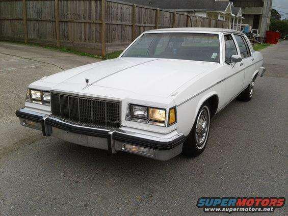 White sedan with chrome grille and trim, wire wheels, parked on asphalt