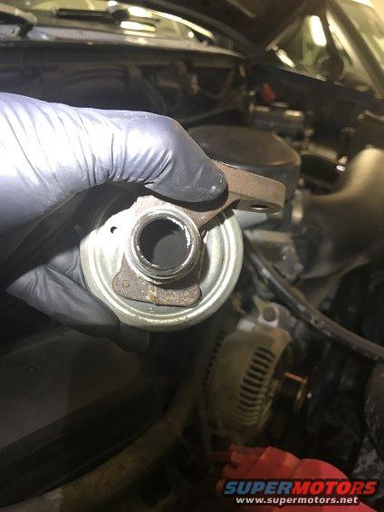 Gloved hand holding a dirty EGR valve with mounting holes