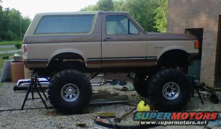 Two-tone brown lifted Ford Bronco on jack stands, side view