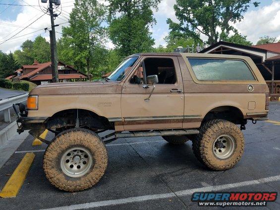 lifted brown Ford Bronco parked on asphalt, side view