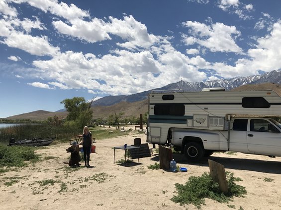 1997 Dodge 3500 camper truck parked on dirt near a lake with mountains in the background