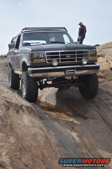 Ford Bronco climbing rocky terrain with a person standing on the hood