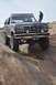 1991 Ford Bronco - A modified Ford Bronco navigates a challenging rocky trail, with a person observing from atop the vehicle.