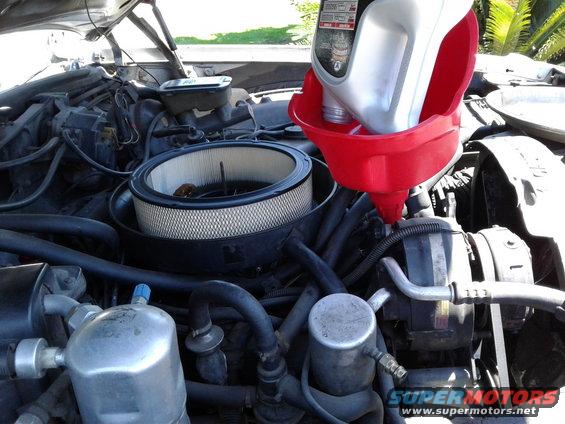 Engine bay of a 1984 Buick Electra with oil being poured into the engine