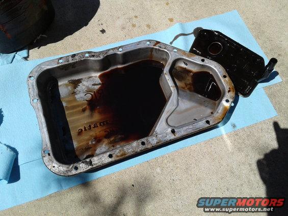 transmission pan with old fluid and a dirty filter next to it