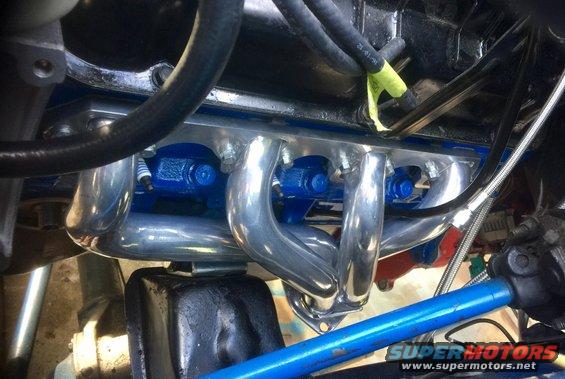 Close-up of shiny exhaust headers and blue engine block with spark plugs visible
