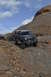 1991 Ford Bronco - A dark gray Ford Bronco navigates a rocky off-road path under a cloudy sky, with another vehicle visible in the background.