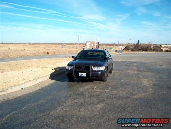 Black 2001 Ford Crown Victoria Police Interceptor parked in a lot, front view. License plate reads ADAM-12