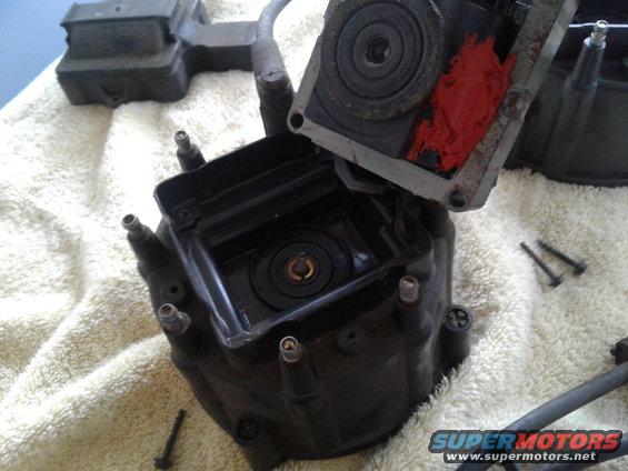 Disassembled black car distributor cap with red sealant and metal rotor on a white towel