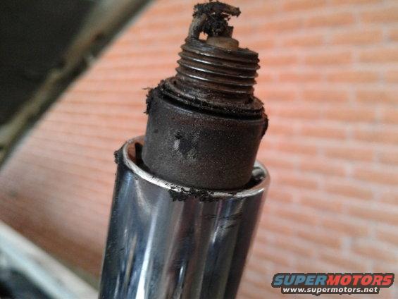 Heavily fouled spark plug with carbon buildup, removed from engine