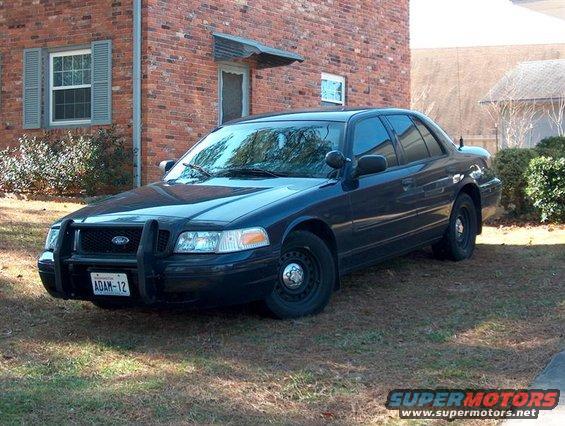 Dark 2001 Ford Crown Victoria with push bar parked in front of brick building