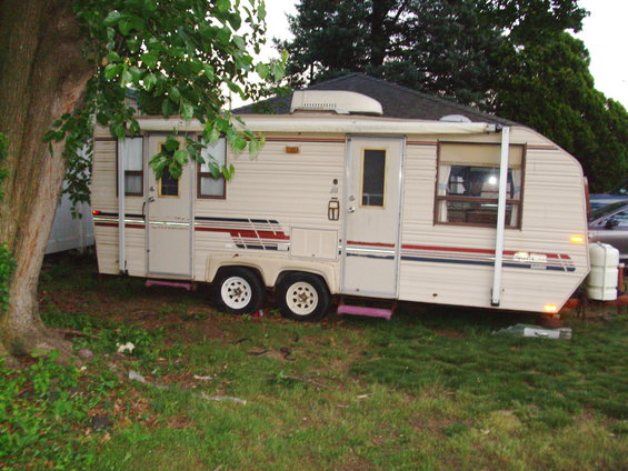 Cream-colored travel trailer with red and blue stripes parked on grass.