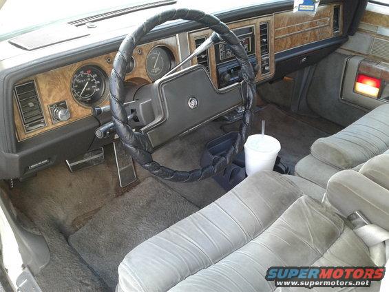 car interior with wood trim, analog gauges, and cloth seats. Cup in holder