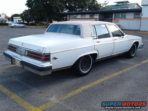 White sedan parked in a lot, rear quarter view. License plate reads 323 IA