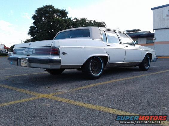 White sedan parked in a lot, rear view. Blue trim on wheels