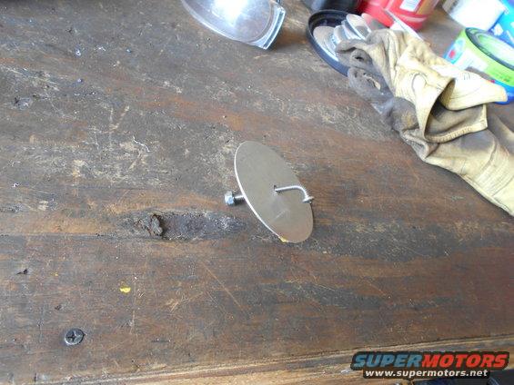 Metal disc with a bolt and hook attached, lying on a wooden workbench