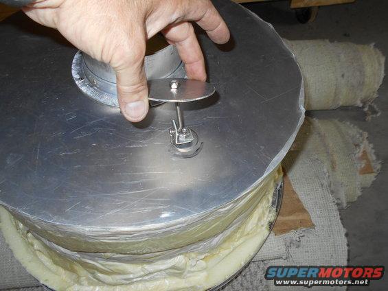 Hand holding a metal disc on a cylindrical object wrapped in insulation