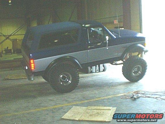 Lifted blue and silver Ford Bronco with a dark blue soft top, parked indoors