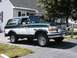 1994 Ford Bronco - A two-tone green and white Ford Bronco is parked in front of a house on a sunny day.