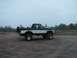 1994 Ford Bronco - This lifted Ford Bronco is shown from the side on a gravelly surface with trees in the background.