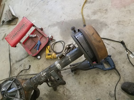 Rear axle assembly, reciprocating saw, Craftsman tool cart, and drill on concrete floor