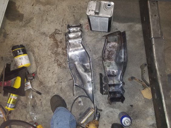 Two metal car parts, one shiny and one rusted, on a concrete floor with tools and cans