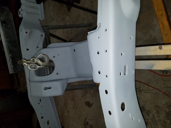 Close-up of a vehicle frame, painted gray, with a tow hook and chain attached