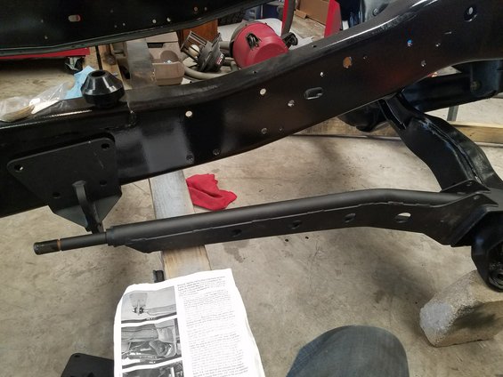Close-up of a vehicle's black painted frame with suspension components and a red rag. Instructions are on the floor
