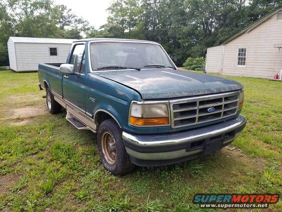 Teal 1996 Ford F-150 pickup truck parked on grass in front of a house and shed