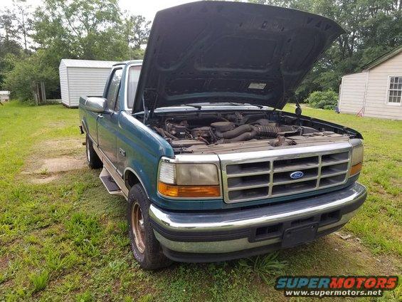 Teal Ford F-Series truck with hood open, showing engine bay. Grille has horizontal bars and a Ford emblem