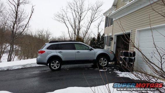 Silver Subaru Outback parked on a wet driveway next to a beige house with an open garage door