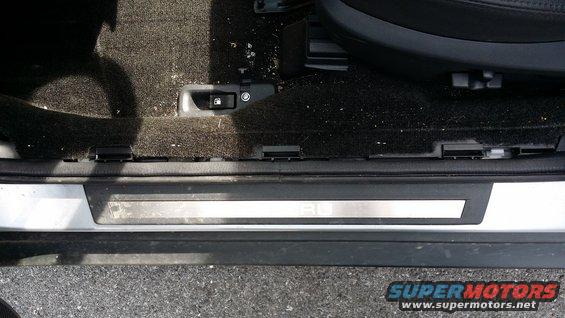 Interior door sill with a silver accent plate reading 'OUTBACK' and a fuel door release button
