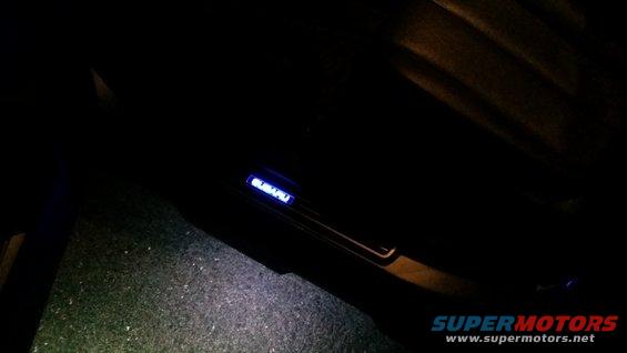 Illuminated Subaru door sill glowing blue inside a dark vehicle interior