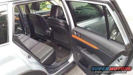 Back seat and doors of a silver car. Black leather seats and wood trim on the doors