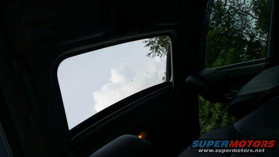Interior view of a car's sunroof open to the sky, with trees visible outside