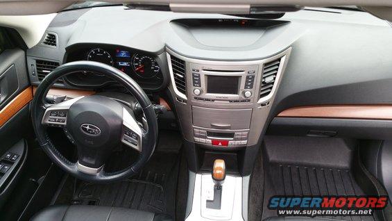 Car interior showing dashboard, steering wheel with Subaru logo, and center console. Wood trim accents are visible