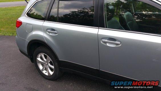 Side view of a silver Subaru Outback. Rear passenger door and wheel are visible