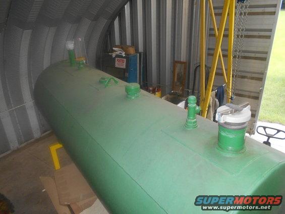 Large green horizontal storage tank with multiple green fittings and a silver cap, inside a corrugated metal building