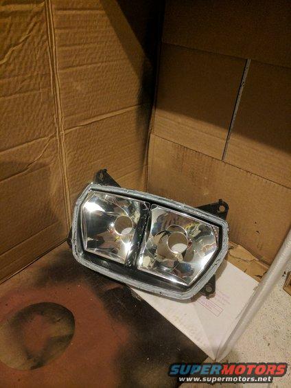Motorcycle headlight assembly with dual clear lenses, mounted on a cardboard background