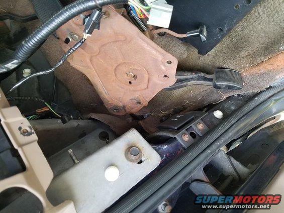 Vehicle interior floor showing pedals, rusty bracket, and wiring harness