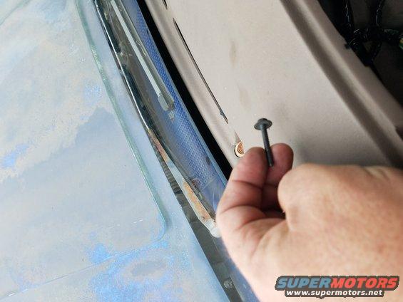 hand holding screw near windshield trim, part of a vehicle interior visible