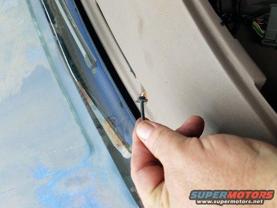 Hand holding a screw near the dashboard trim of a vehicle