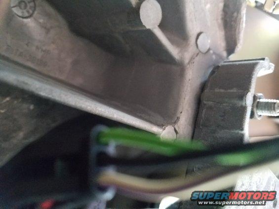 Close-up of green and white wires connected to a metal bracket on a vehicle